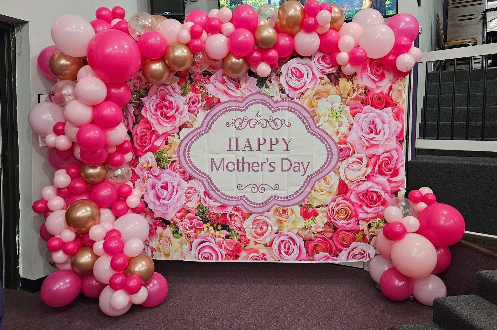 Pink and rose gold balloon garland framing a floral Mother's Day backdrop